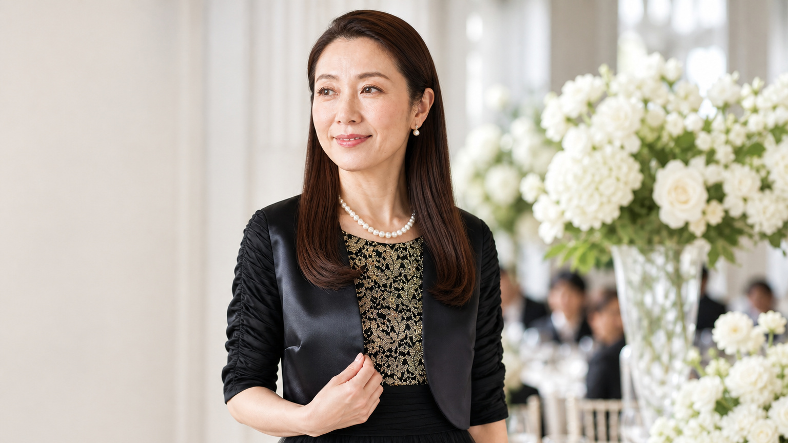 明るい披露宴会場で、黒のドレスとボレロを着た新婦の母