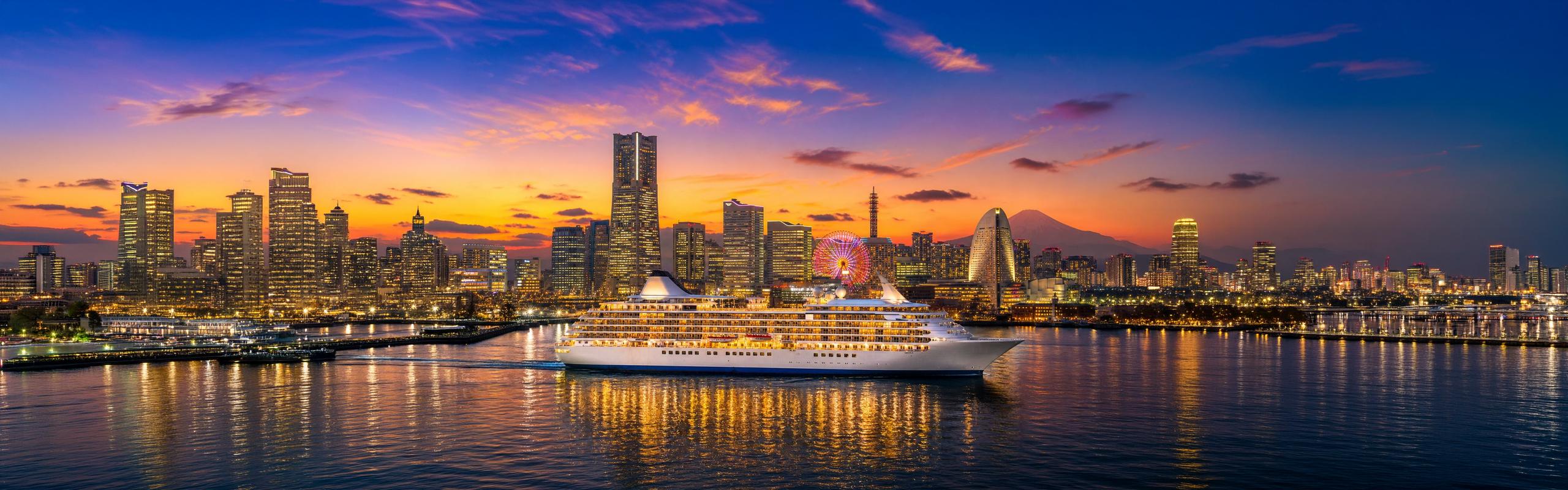黄金色に染まる夕空の下、みなとみらいの夜景を背に横浜の海を進む豪華客船